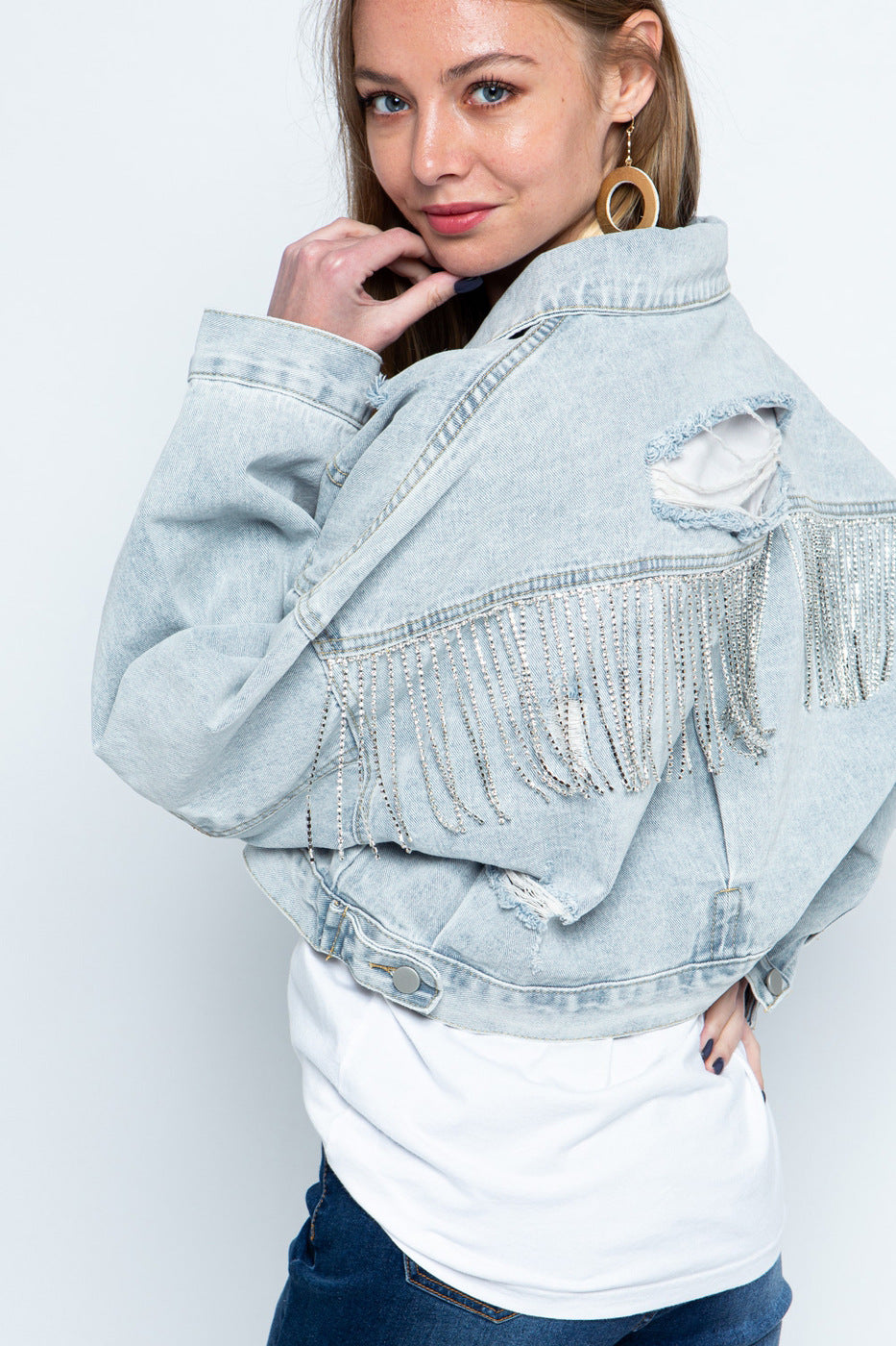 Stylish denim jacket for women with ripped details, rhinestone embellishments, tassel accents, and long sleeves.